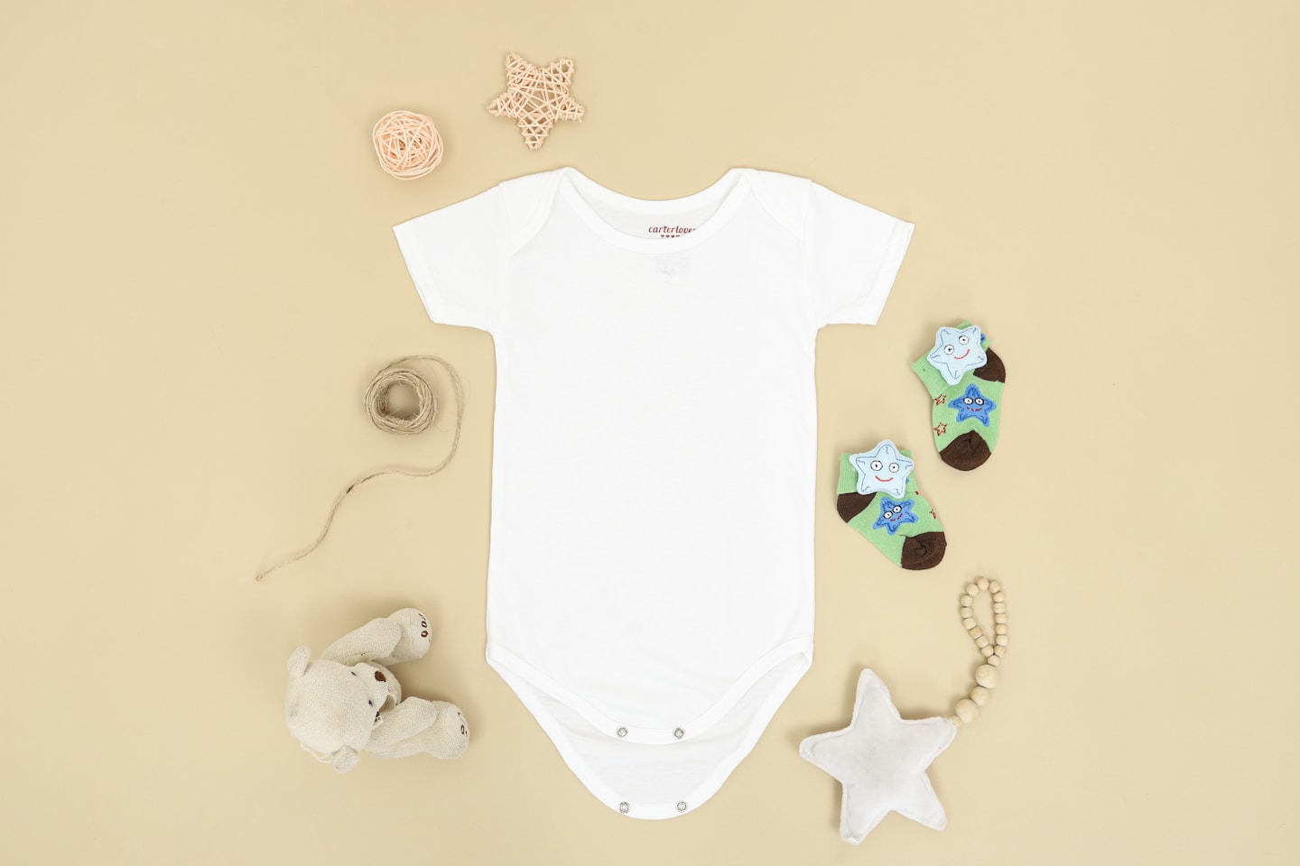 A flatlay baby onesie mockup scene featuring a onesie lying on the ground next to toys and cute small socks