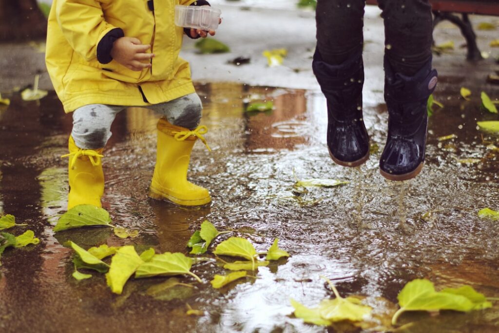 Deux enfants en bottes de pluie qui sautent dans une flaque couverte de feuilles d’automne
